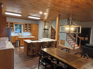 Eine geräumige Küche mit Holzausbau, einer zentralen Kochinsel und einem Essbereich mit großem Holztisch und Stühlen.