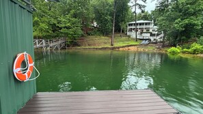 A wooden dock extending over a calm body of water, a lifebuoy attached to a green wall, and a two-story building with a balcony in the background. - Family. Porches. Pets. Smith Lake. "Just Heavenly" (Arley)