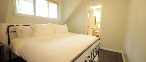 A bedroom with a bed, a window, a ceiling fan, and a door leading to another room.
