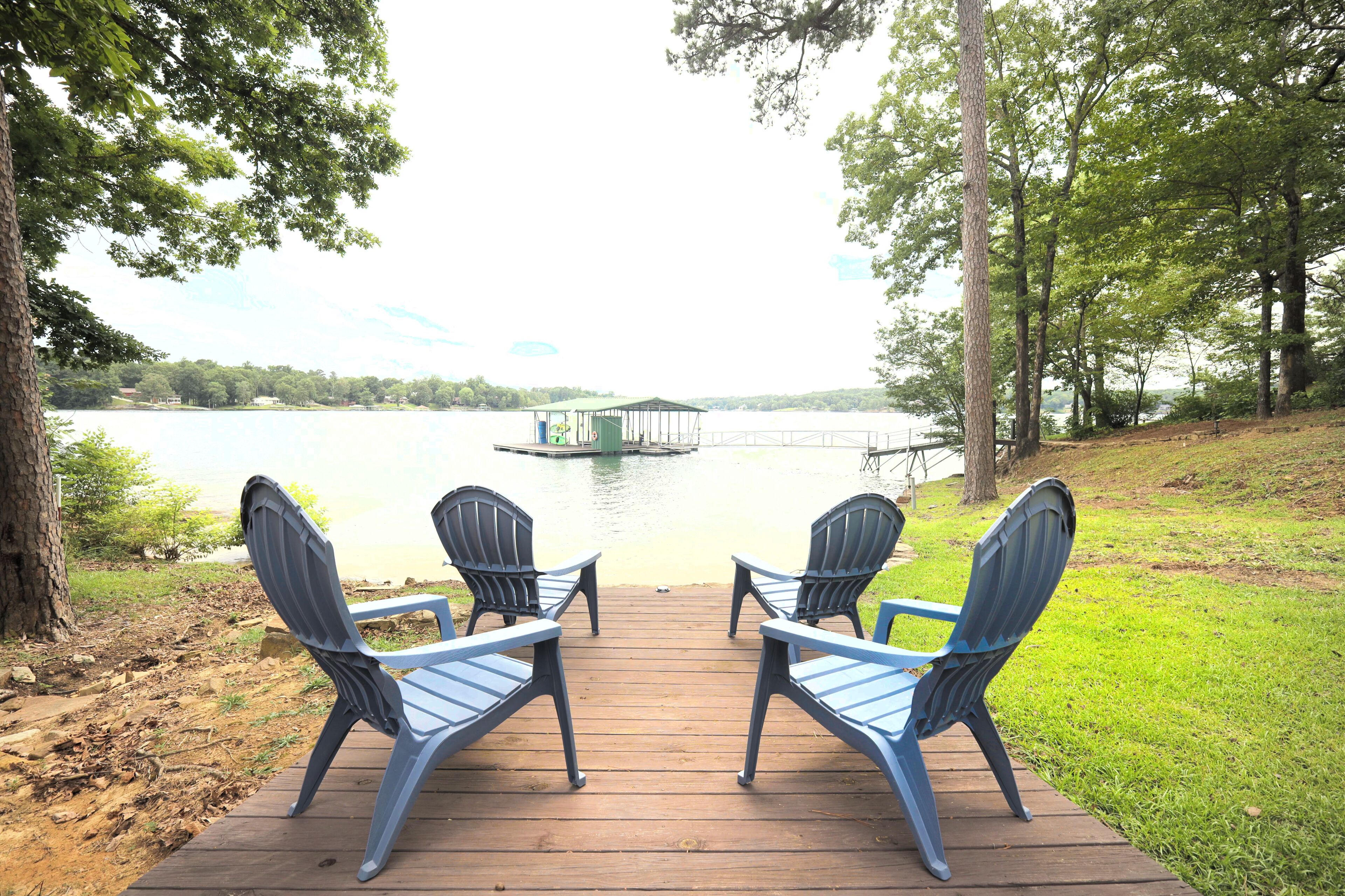 Eine Holzterrasse mit zwei Adirondack-Stühlen, die auf einen See blicken, einem Steg und einem Gazebo.