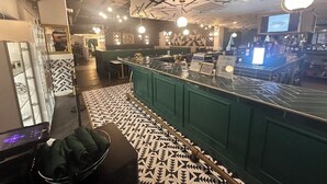 Una zona de bar con mostrador verde, suelo estampado y techo con diseños geométricos.