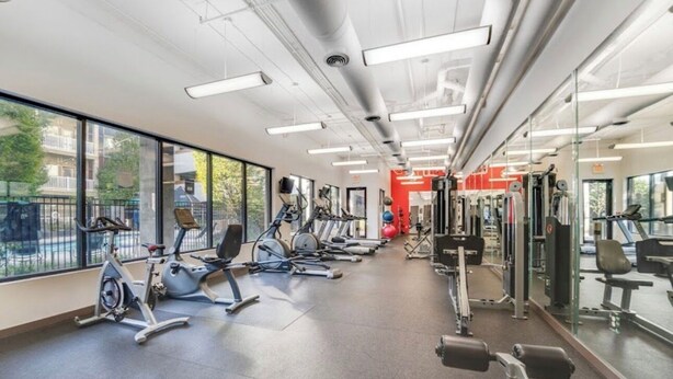 Un gimnasio con equipamiento de ejercicio, amplias ventanas y un espejo grande.