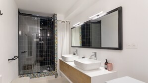 Casa de banho moderna com cabine de duche em vidro, duas pias, um espelho grande e um lavatório branco.