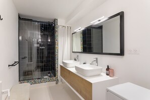 Ein modernes Badezimmer mit Duschkabine aus Glas, zwei Waschbecken, einem großen Spiegel und einem weißen Waschtisch.
