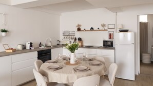 Uma cozinha moderna com armários brancos, uma mesa de jantar posta para seis pessoas e uma pequena ilha com um vaso de flores.