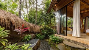 A tropical resort with a thatched-roof structure, a stone pathway, and a glass-enclosed room with a view of the surrounding greenery. - Cacao House Eco-luxe Family Home Near Green School (Abiansemal)