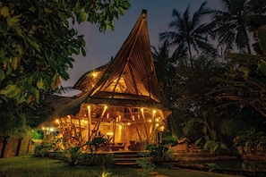 A wooden structure with a sloped roof, surrounded by lush greenery and palm trees. - Cacao House Eco-luxe Family Home Near Green School (Abiansemal)