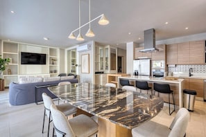 A modern kitchen with a central island, built-in appliances, and a dining area with a glass-top table. - Peaceful Condo With Resort Pool, High-speed Wifi & Relaxing Outdoor Space (Cabo San Lucas)