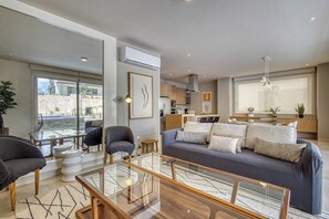 A modern living room with a glass coffee table, a sofa with cushions, a dining area with a glass table, and a kitchen in the background. - Peaceful Condo With Resort Pool, High-speed Wifi & Relaxing Outdoor Space (Cabo San Lucas)