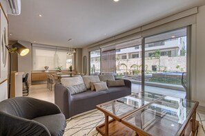 A modern living room with a sofa, a glass coffee table, and a dining area with a table and chairs. - Peaceful Condo With Resort Pool, High-speed Wifi & Relaxing Outdoor Space (Cabo San Lucas)