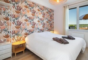 A bedroom with a bed, a nightstand, a lamp, and a window with a view. - Gîtes de France® - La Villa Pomponette (CRIEL SUR MER)