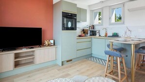 A modern kitchen with a TV, a microwave, and a dining area with stools. - Gîtes de France® - La Villa Pomponette (CRIEL SUR MER)