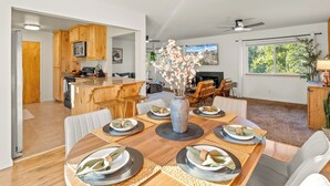 A modern kitchen with wooden cabinets, a dining area with a wooden table set for four, and a living room with a fireplace and seating. - NEW Hot Tub-Fire Pit-Arcade Game-BBQ (Mariposa)