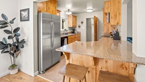 A modern kitchen with wooden cabinets, a stainless steel refrigerator, granite countertops, and a potted plant. - NEW Hot Tub-Fire Pit-Arcade Game-BBQ (Mariposa)
