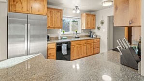 A kitchen with wooden cabinets, a stainless steel refrigerator, granite countertops, and a dishwasher. - NEW Hot Tub-Fire Pit-Arcade Game-BBQ (Mariposa)