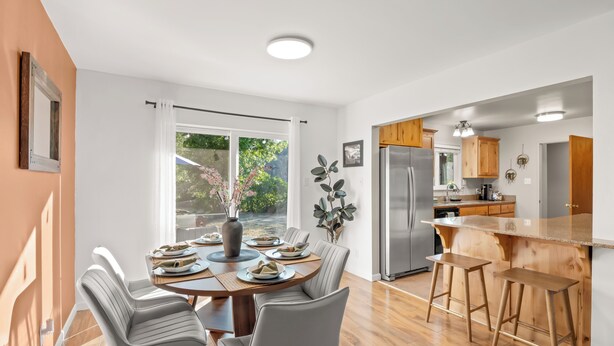 A modern kitchen with a large island, wooden cabinets, and a dining area with a table set for four. - NEW Hot Tub-Fire Pit-Arcade Game-BBQ (Mariposa)