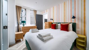 Ein modernes Hotelzimmer mit einem großen Bett, einem Nachttisch, einem Kleiderschrank, einem Fenster mit Vorhängen und einer Wand mit Punkte-Muster.