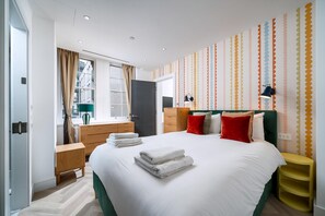 Ein modernes Hotelzimmer mit einem großen Bett, einem Nachttisch, einem Kleiderschrank, einem Fenster mit Vorhängen und einer Wand mit Punkte-Muster.