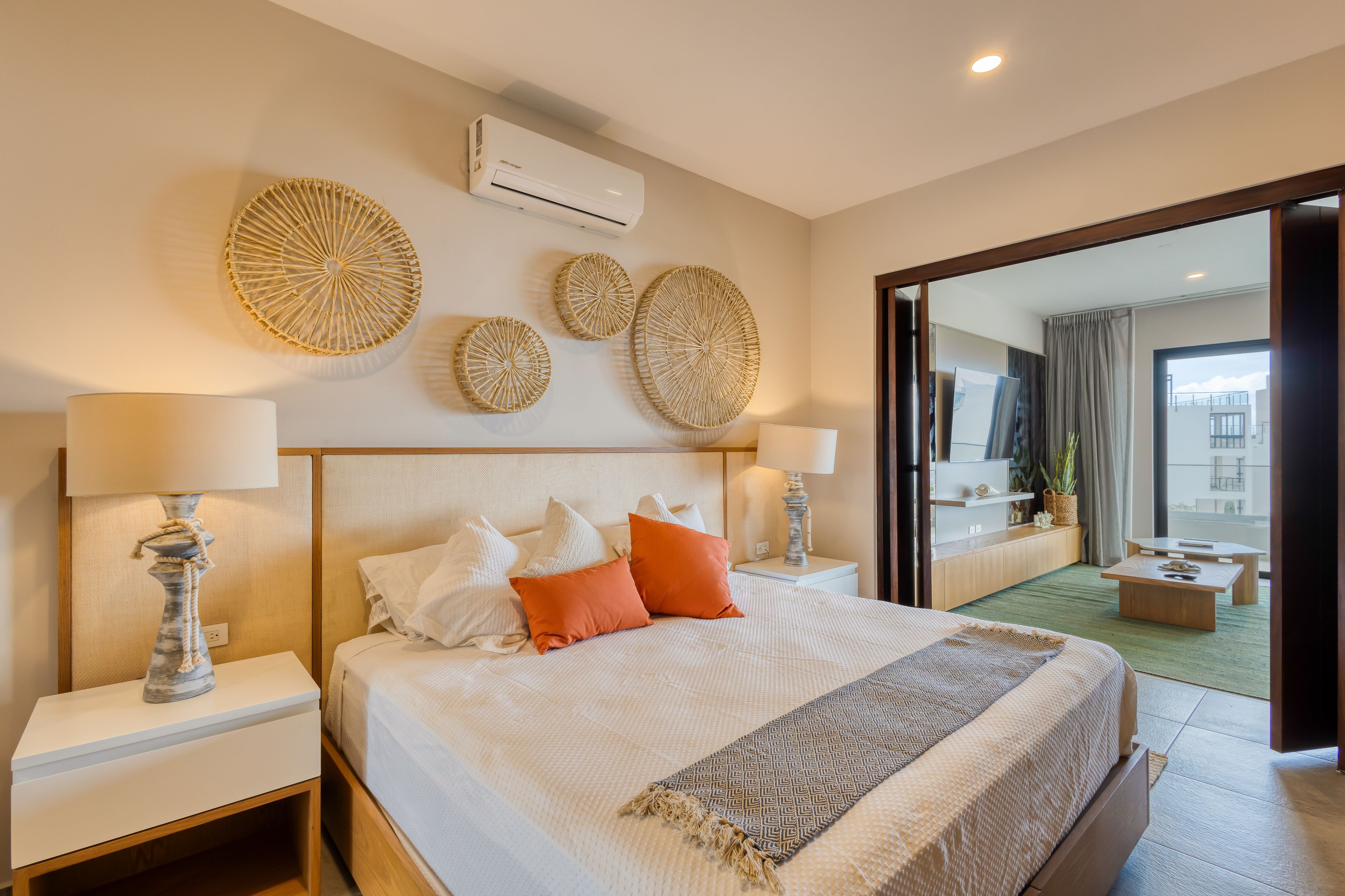 A modern hotel room with a large bed, two bedside tables with lamps, a wall-mounted air conditioner, and decorative wall art.