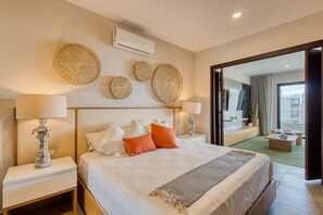 A modern hotel room with a large bed, two bedside tables with lamps, a wall-mounted air conditioner, and decorative wall art. - Peaceful Coastal Stay With Pool, Balcony & Fitness Center (Cabo San Lucas)