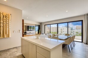 A modern kitchen with a large island, dining area, and large windows offering a city view. - Peaceful Coastal Stay With Pool, Balcony & Fitness Center (Cabo San Lucas)