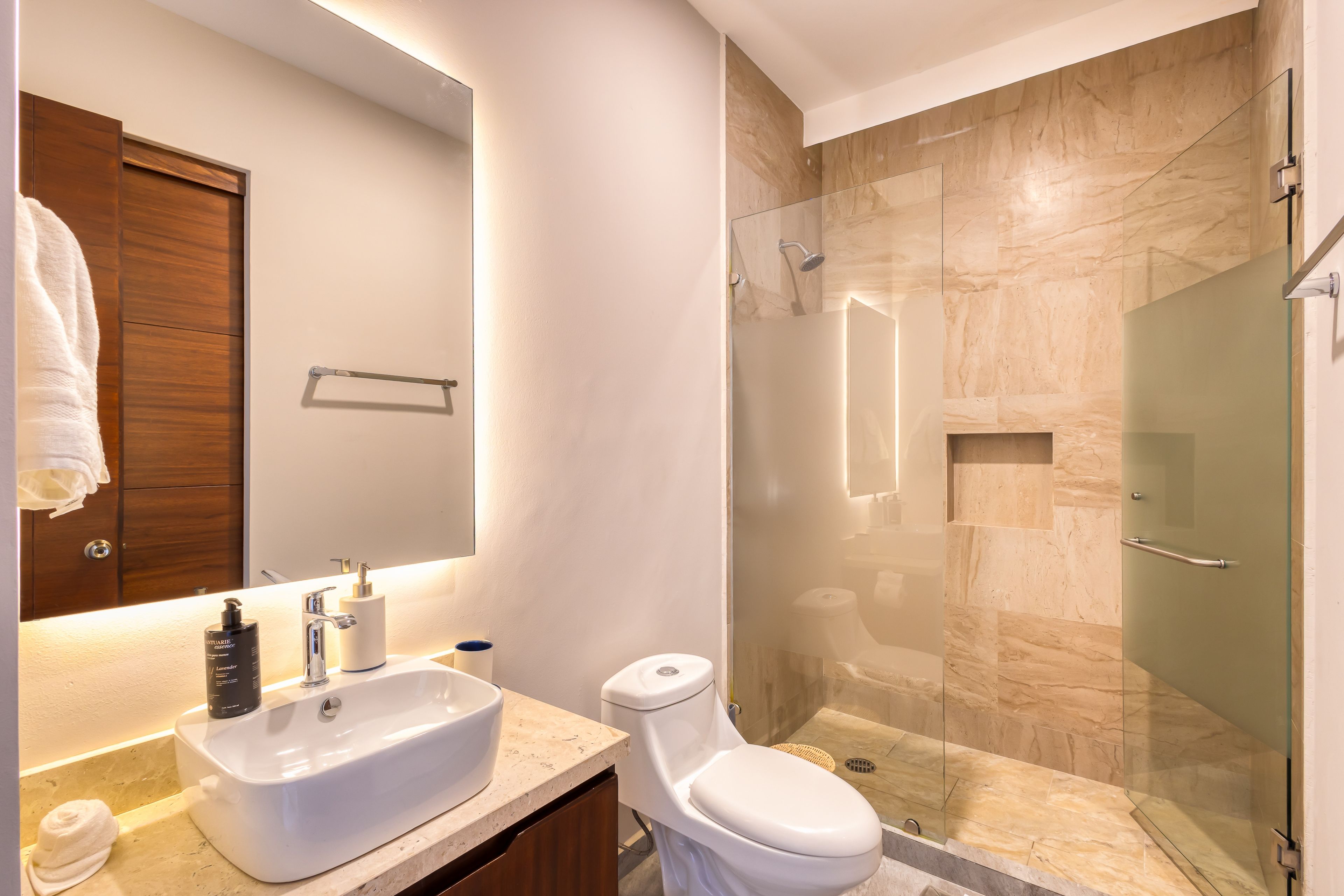 Un baño moderno con lavamanos, inodoro y ducha con mampara de vidrio.