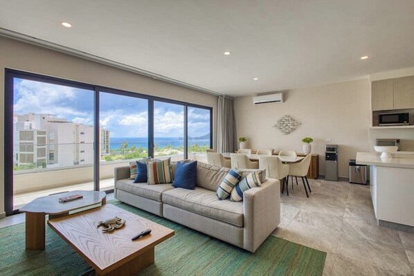 A modern living room with a sofa, coffee table, and dining area. - Peaceful Coastal Stay With Pool, Balcony & Fitness Center (Cabo San Lucas)