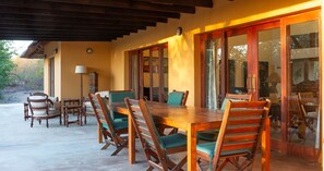 Une terrasse couverte avec une table et des chaises en bois, une lampe et une vue sur l’extérieur.