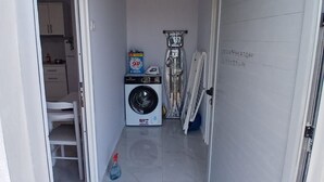 Un couloir étroit où l’on trouve une machine à laver, une serpillière et une porte portant un numéro.