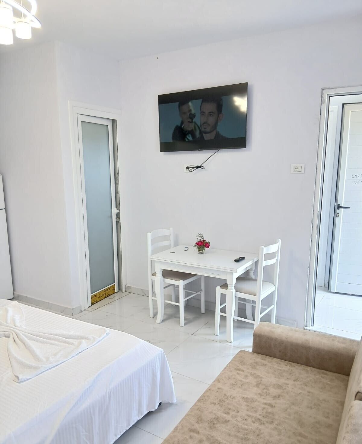 A hotel room with a bed, a small table with chairs, a TV mounted on the wall, and a door.