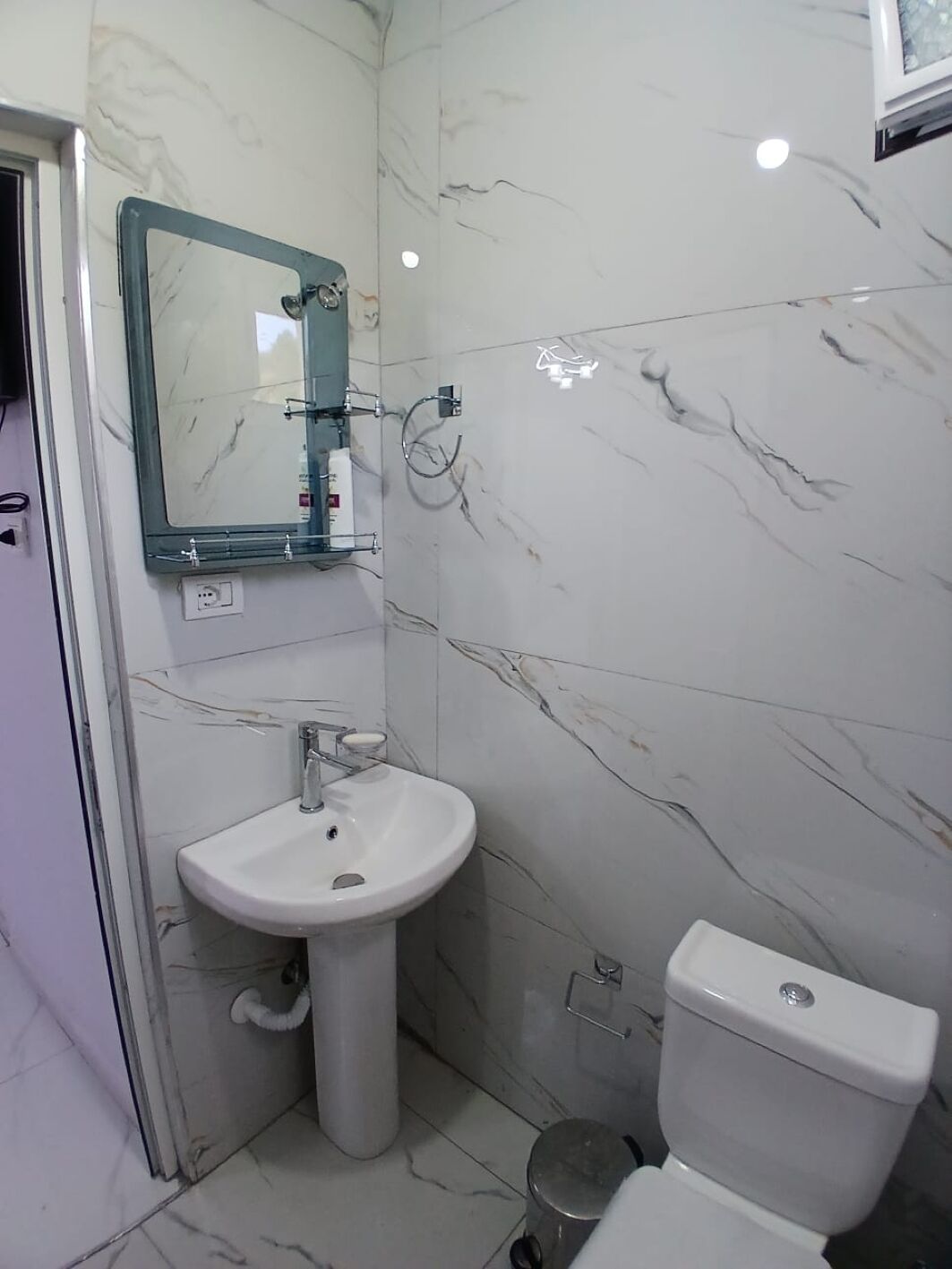 A bathroom with a white sink, a mirror, a toilet, and a marble wall.