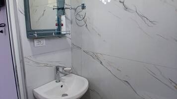 A bathroom with a white sink, a mirror, a toilet, and a marble wall.