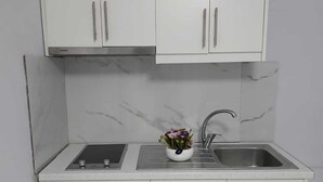 Une cuisine avec des meubles blancs, un pare-feu en marbre, un évier et un petit plan de travail.