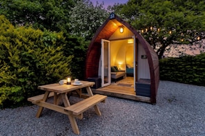 Een gezellig, eenkamerhutje met een houten gevel, een klein terras en een picknicktafel.