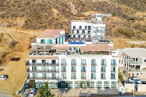 A multi-story hotel with balconies, a rooftop terrace, and a view of a hilly landscape. - Cerro Colorado Studio Condo in Cabo San Lucas (Cabo San Lucas)