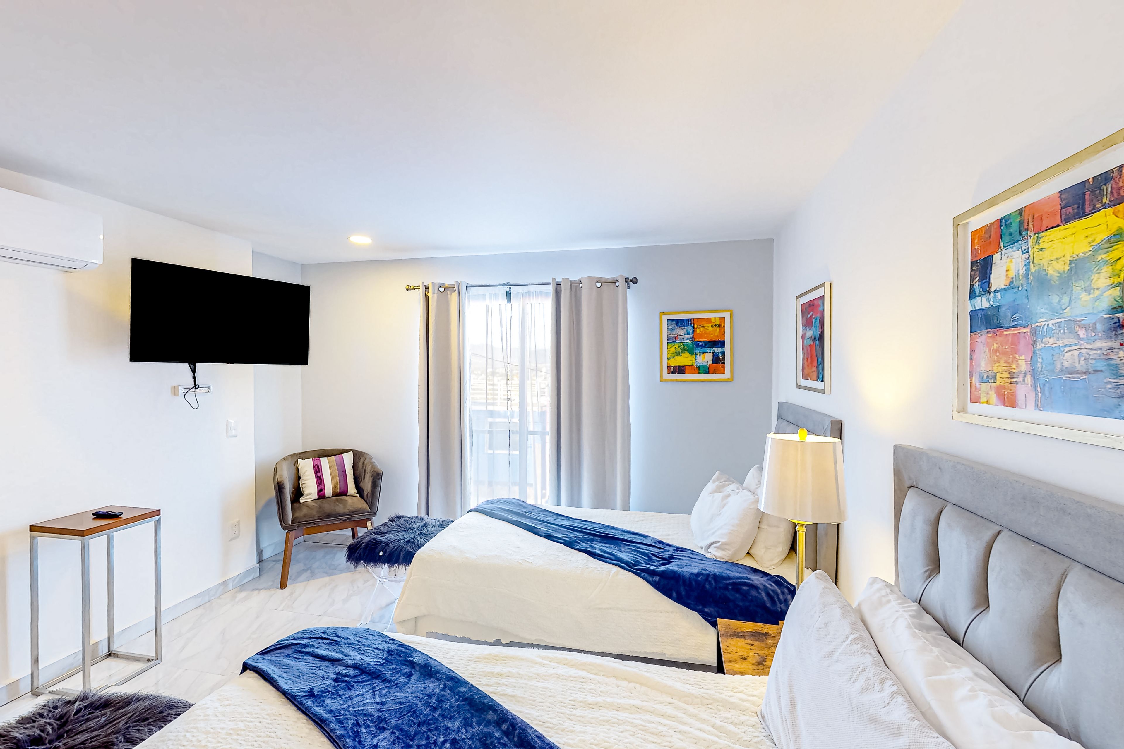 Een hotelkamer met een bed, een televisie, een stoel, een lamp en kunstwerken aan de muren.