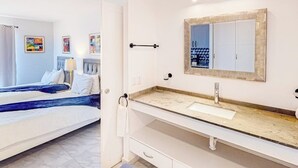 A hotel room with a bed, a bathroom with a sink and mirror, and artwork on the walls. - Cerro Colorado Studio Condo in Cabo San Lucas (Cabo San Lucas)