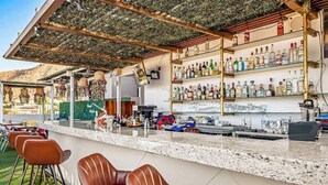 A bar area with a counter, bar stools, and shelves of liquor bottles. - Cerro Colorado Studio Condo in Cabo San Lucas (Cabo San Lucas)