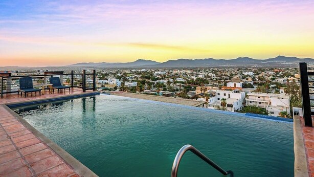 An infinity pool with a cityscape view, a poolside area with chairs, and a clear sky. - Cerro Colorado Studio Condo in Cabo San Lucas (Cabo San Lucas)