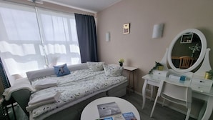 Ett sovrum med en säng, ett skrivbord, en stol, en spegel och ett fönster med gardiner.