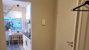 En hall som leder in till ett kök med ett matbord och stolar, en klädhängare och ett kors på väggen.