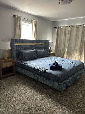 A bedroom with a bed, two bedside tables, a window with curtains, and a carpeted floor. - Awesome 6-bedroom house with AC in vibrant Detroit (Detroit)