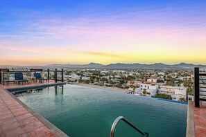 Ein Infinity-Pool auf dem Dach mit Blick auf die Stadt, einer Brüstung und einigen Liegestühlen.