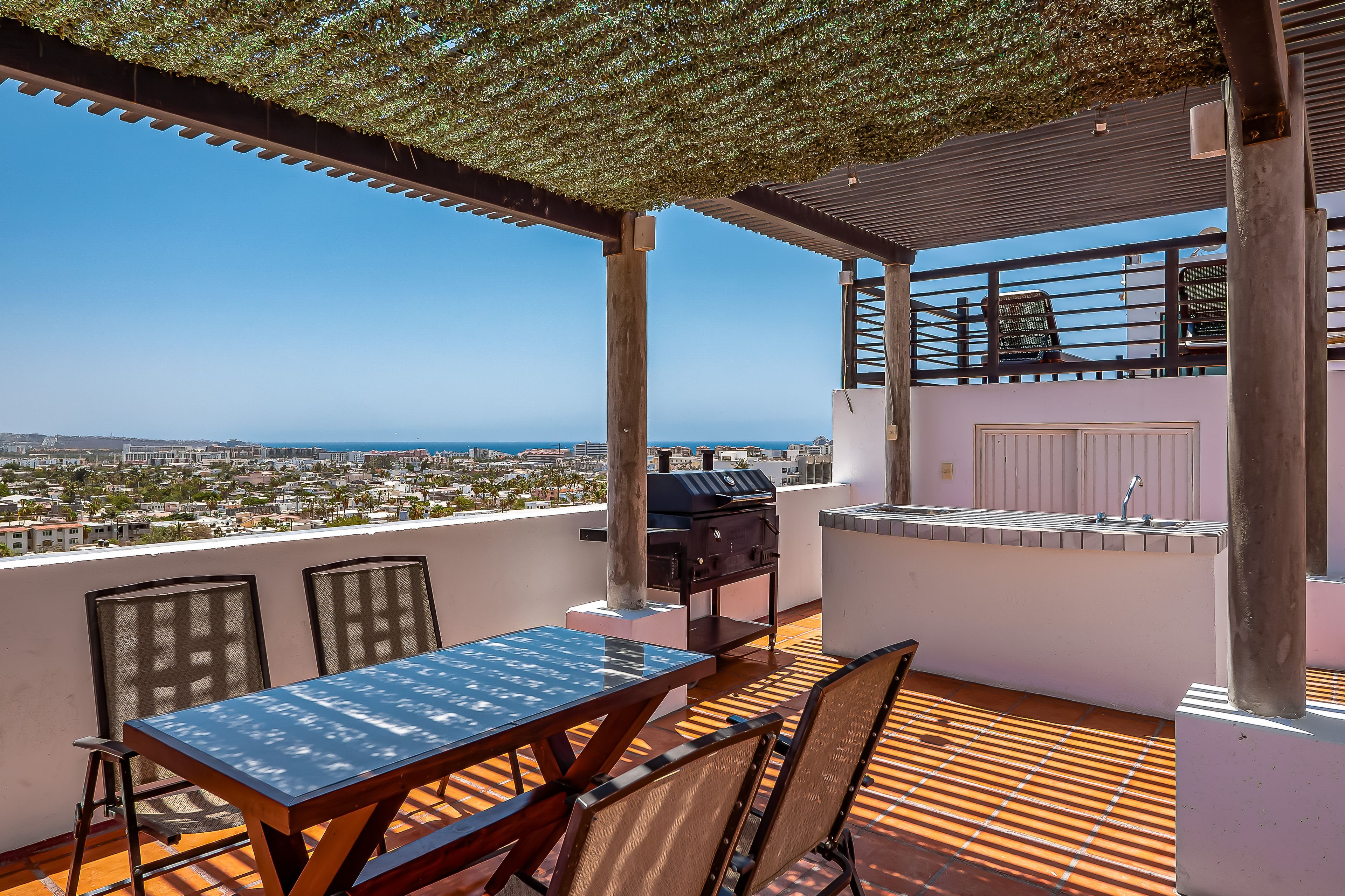 An outdoor patio with a table and chairs, a grill, and a view of the city and sea.