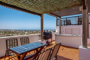 An outdoor patio with a table and chairs, a grill, and a view of the city and sea. - Cerro Colorado Condo Condo in Cabo San Lucas (Cabo San Lucas)