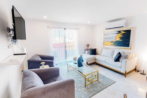 Un salon moderne avec un téléviseur à écran plat, un canapé, une table basse et un tableau accroché au mur.