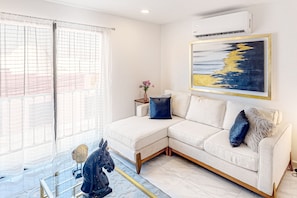 A modern living room with a white sectional sofa, a glass coffee table, and a mounted air conditioner. - Cerro Colorado Condo Condo in Cabo San Lucas (Cabo San Lucas)