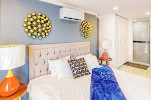 Ein Schlafzimmer mit einer gesteppten Kopfstütze, einem Bett mit weißen und gemusterten Kissen, einer blauen Tagesdecke und zwei kugelförmigen Wanddekorationen.