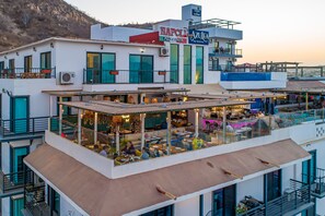 Un edificio de varios pisos con bar y comedor en la azotea, que cuenta con un restaurante llamado Napoli Pizza & Pasta y otro llamado Azul.