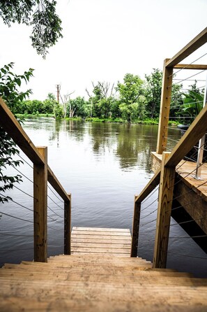 Un escalier en bois mène à une jetée surplombant une étendue d’eau calme, avec une végétation luxuriante en arrière-plan.